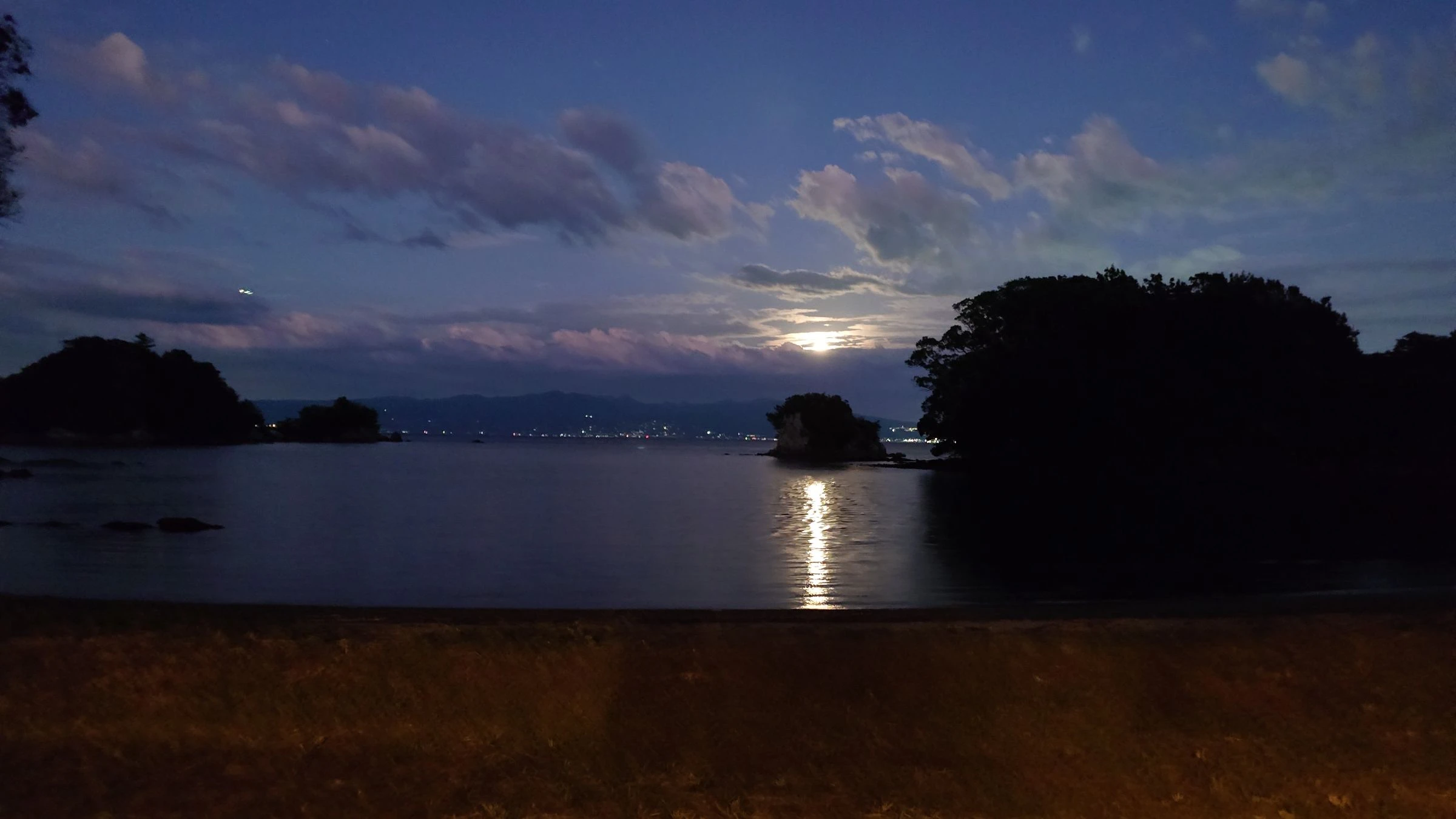 島影の向こうに浮かぶ月と、海に伸びる月明かり