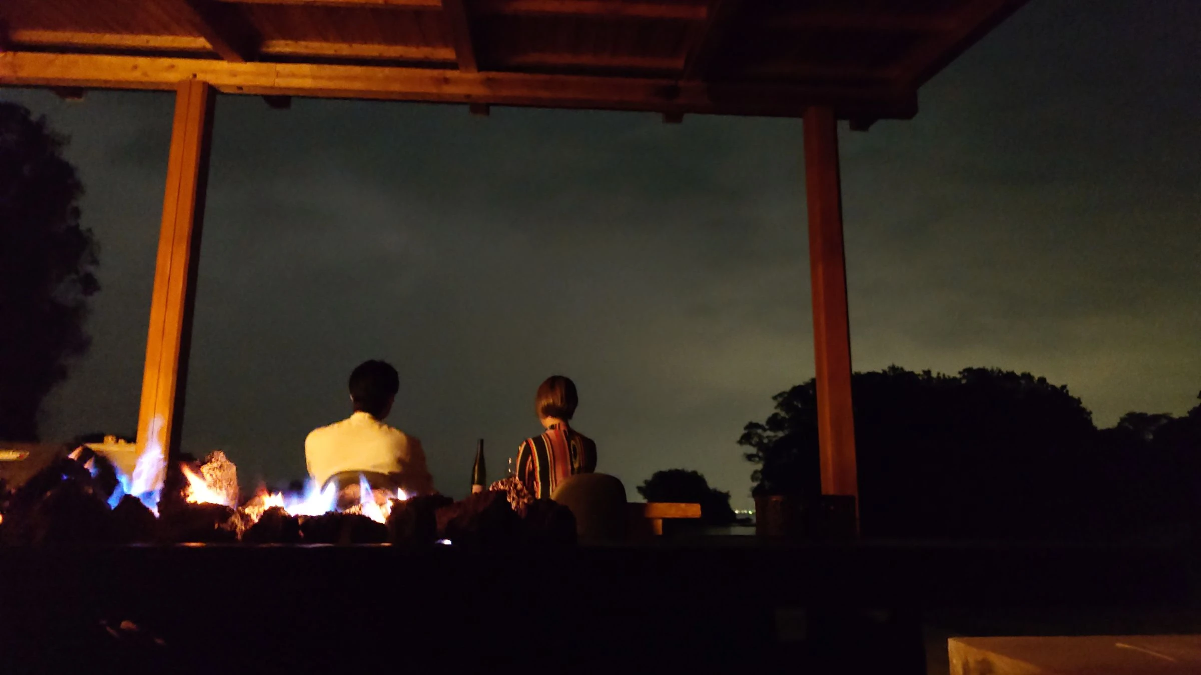火を前に並んで座り、夜の海を眺めるふたりの後ろ姿