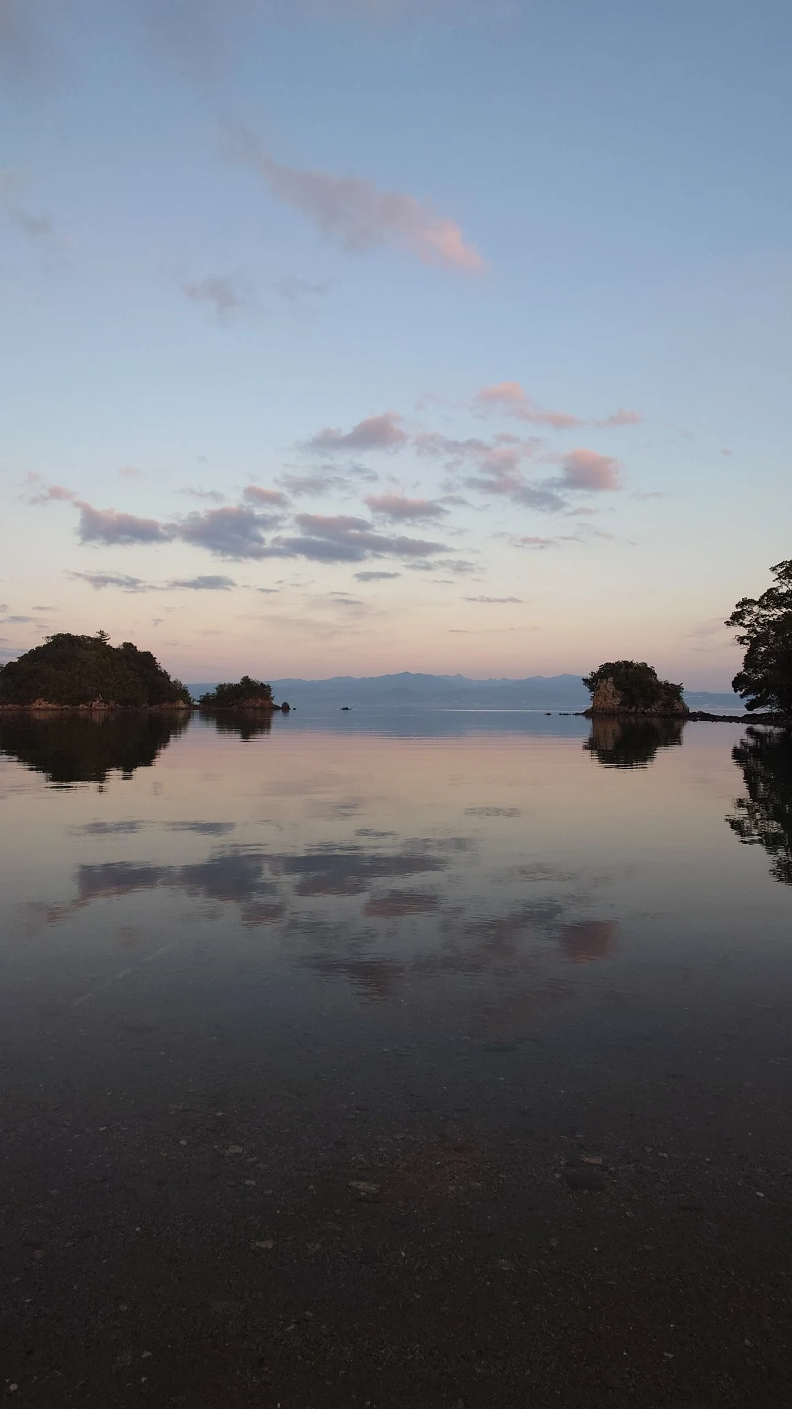 夕方、島影と淡い空を鏡のように映す海
